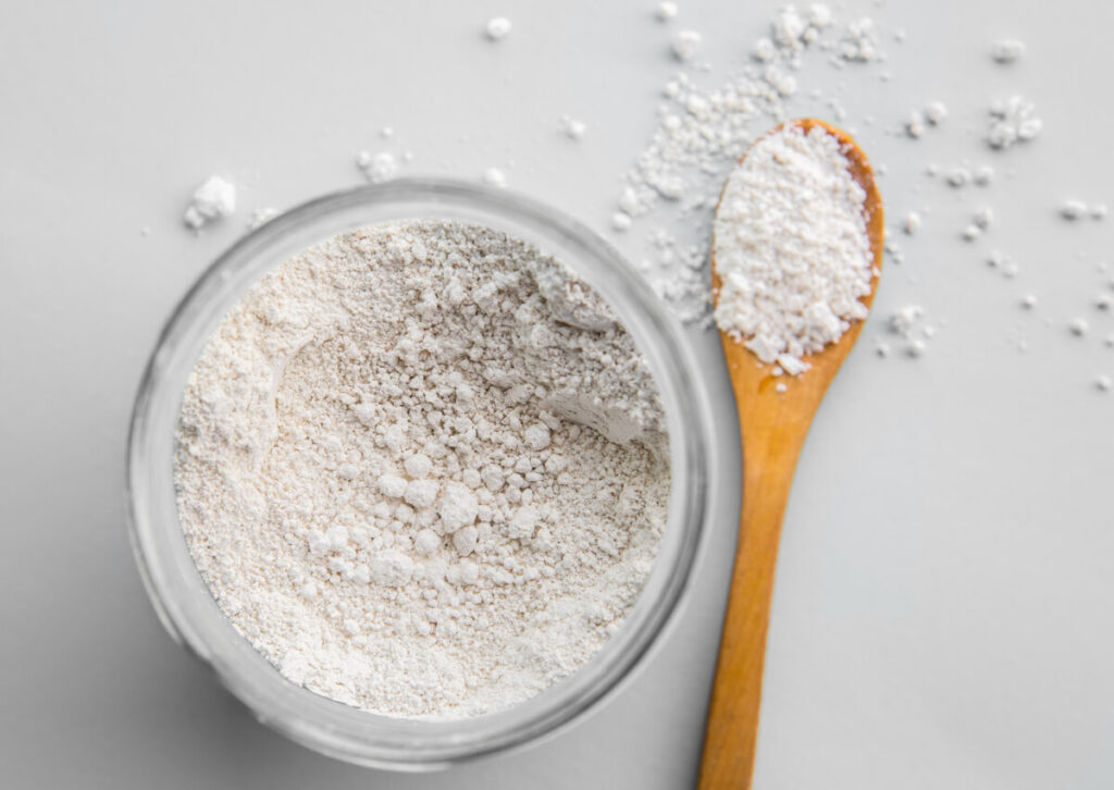 Diatomaceous earth also known as diatomite mixed in glass jar and wood spoon on gray background